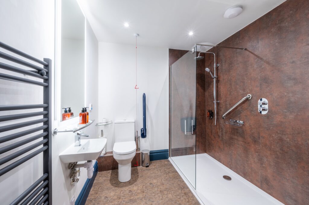 Modern bathroom suitable for a disabled person, with handles and a seat in the large shower cubicle and a handle next to the toilet.