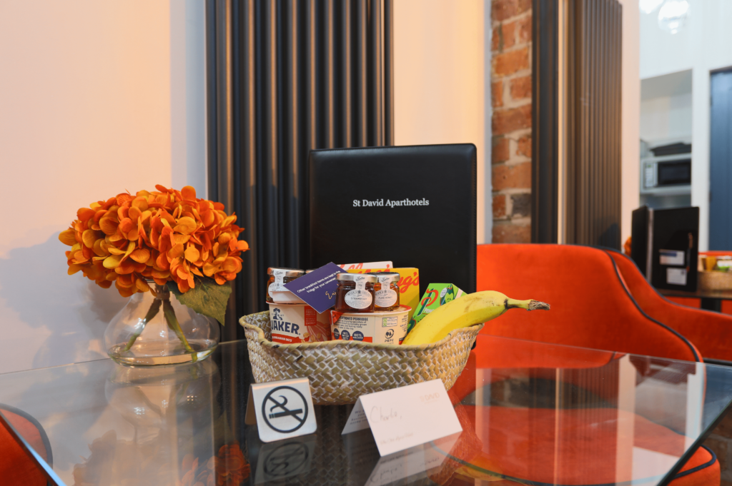 Table with a basket of snacks, a no smoking sign, a vase of orange flowers, and a menu labeled "St David Aparthotels".